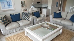 Un salon avec deux canapés beiges, dont l’un est agrémenté de coussins à motifs, une table basse en verre et un tapis tissé.