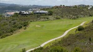 Un parcours de golf avec un chemin sinueux, entouré d’une végétation luxuriante et bordé, au loin, par des immeubles résidentiels.