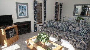 A living room with a sofa, a coffee table with a plant, a television on a stand, and a fireplace. - Villa 9 (Knysna)