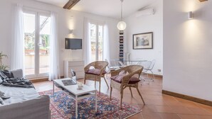A modern living room with a sofa, a coffee table, wicker chairs, a dining table with chairs, a TV, and a bookshelf. - Monti Stairway to Heaven (Rome)