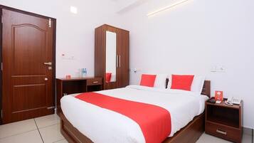 Une chambre d’hôtel avec un grand lit, une armoire, une table de chevet avec une lampe et une petite table avec un téléphone et une boîte rouge.