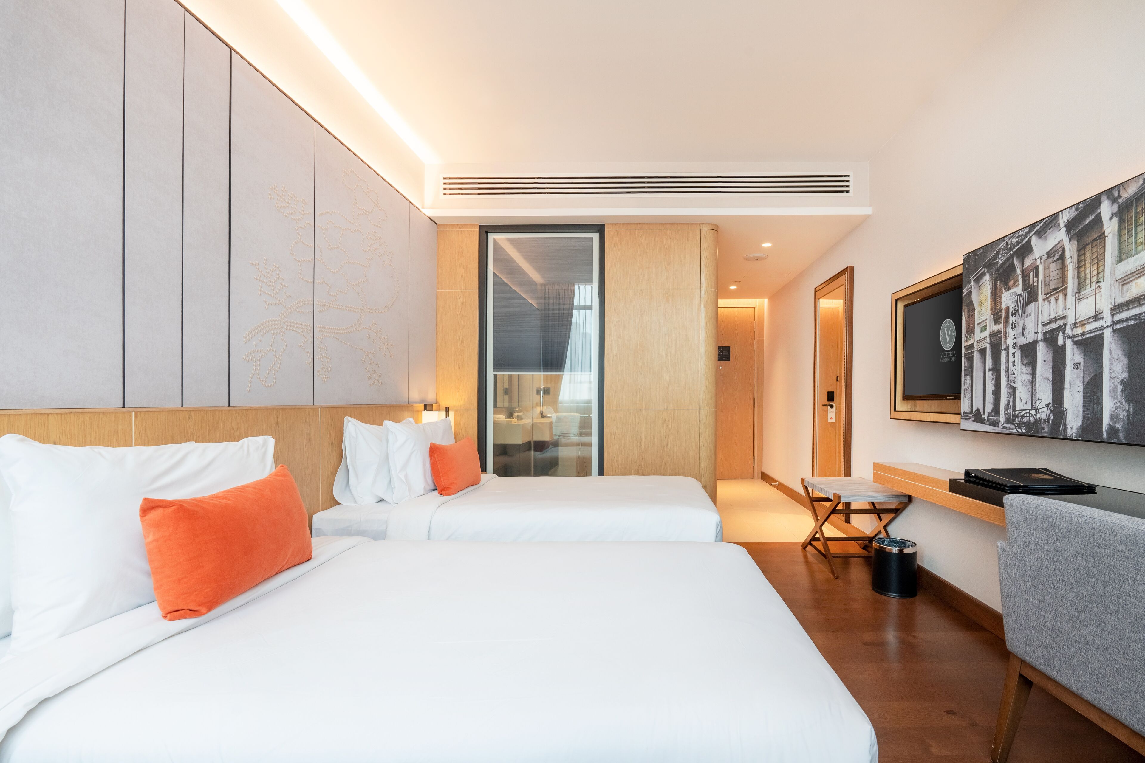 A hotel room with two beds, a desk, a chair, a television, and a large window.