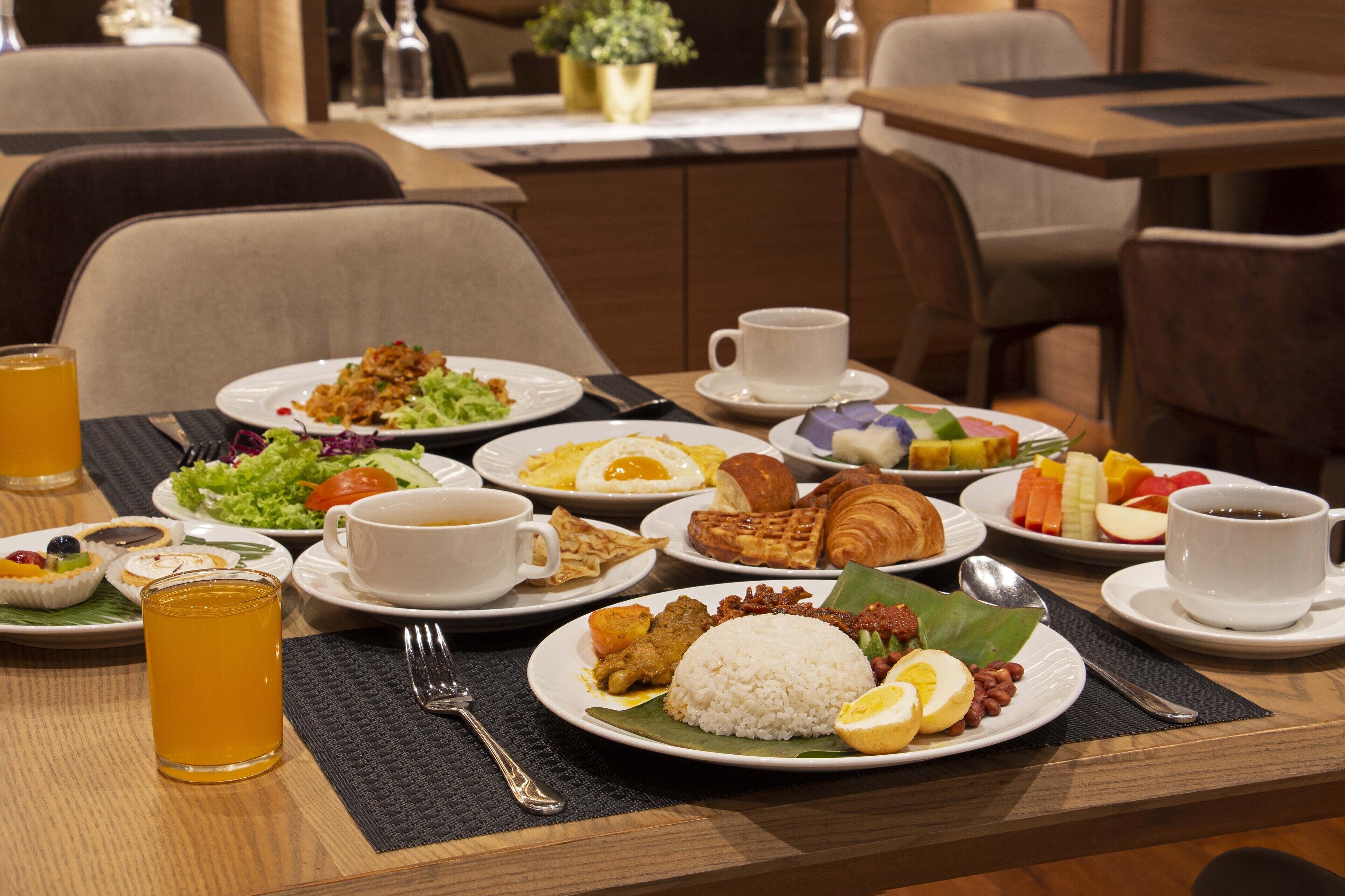 A breakfast buffet with various dishes, including rice, eggs, and pastries, and a glass of orange juice.