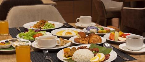 A breakfast buffet with various dishes, including rice, eggs, and pastries, and a glass of orange juice.