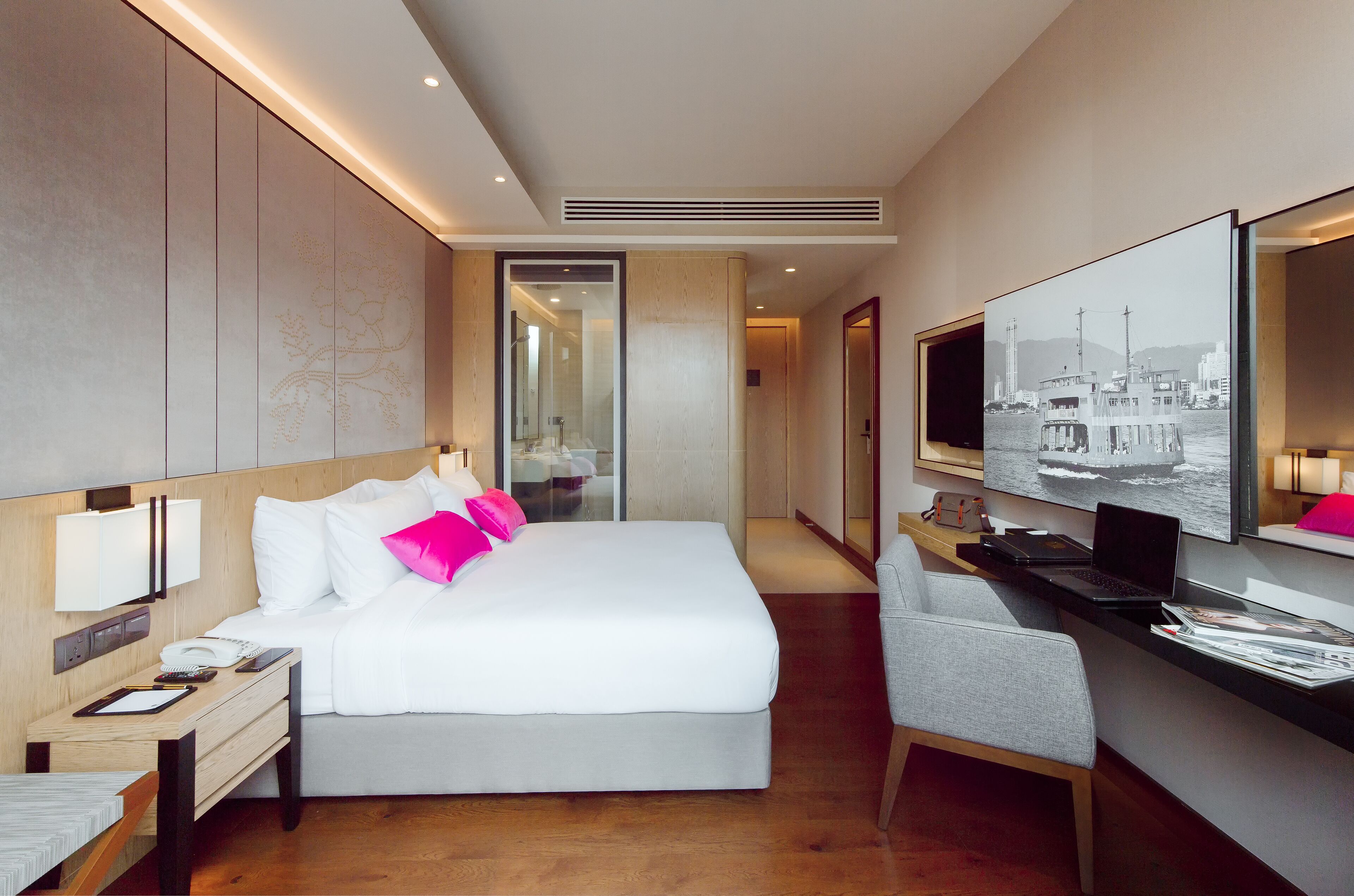 A modern hotel room with a large bed, a desk with a laptop, a chair, and a TV mounted on the wall.