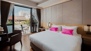 A hotel room with a large bed, a desk with a chair, a small table, and a view of buildings outside through a large window. - Victoria Garden Hotel (George Town)