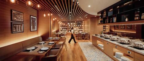 A restaurant with wooden panel walls, hanging pendant lights, and a central dining area with tables and chairs.