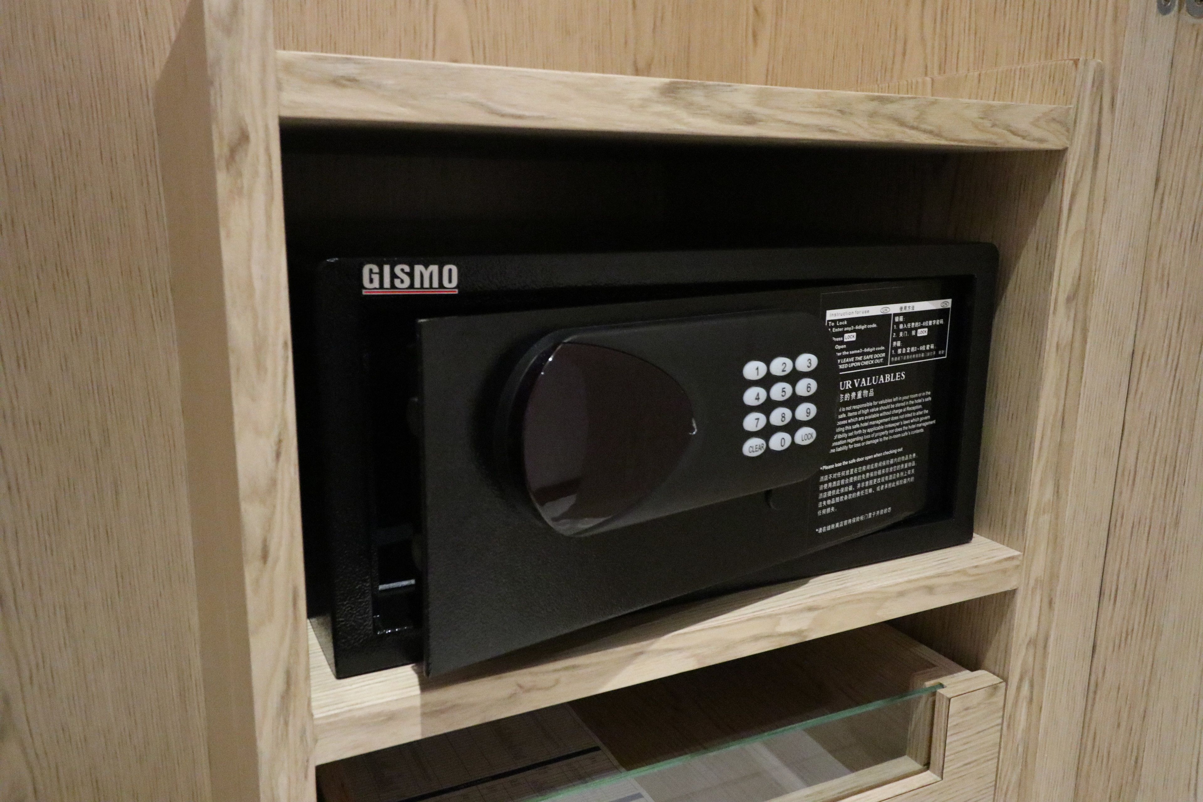 A black security system with a keypad and a display screen, housed in a wooden cabinet with a glass door.