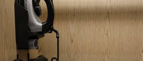 A wall-mounted iron with a cord, a power outlet, and a wooden panel.
