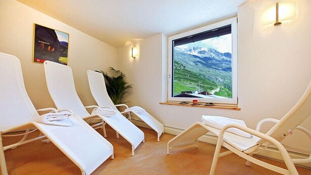 Een kamer met vier witte ligbedden, een groot raam met uitzicht op bergen, en een lijst met een afbeelding aan de muur.