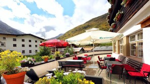 Een terras buiten met rode en witte parasols, rode en zwarte stoelen en bloempotten.