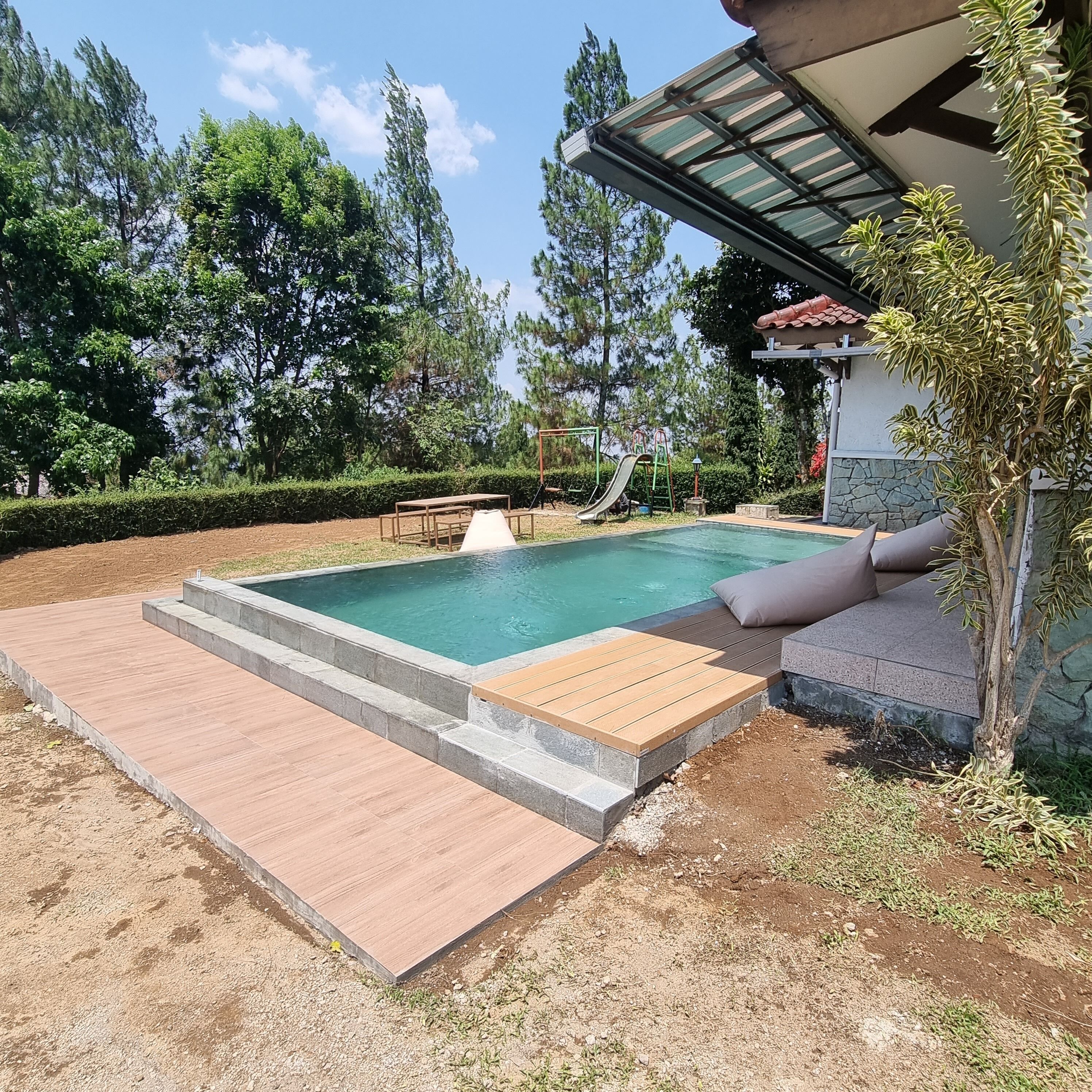 Una piscina con muelle de madera, un tobogán y una pequeña mesa.