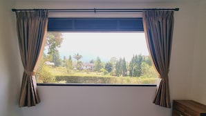 Une chambre avec une grande fenêtre, des rideaux, un lit et une commode en bois.
