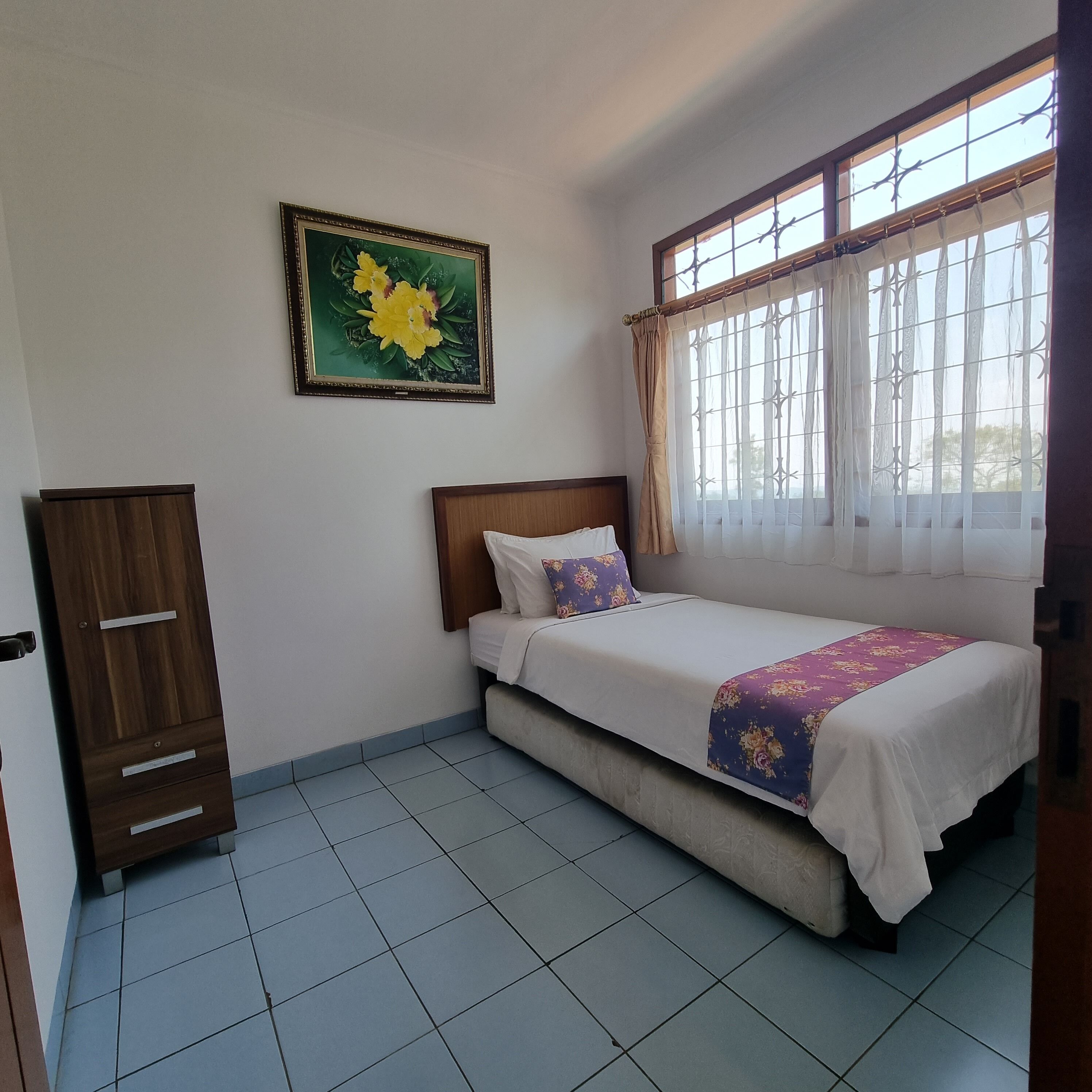 A bedroom with a bed, a wardrobe, a window with curtains, and a painting on the wall.