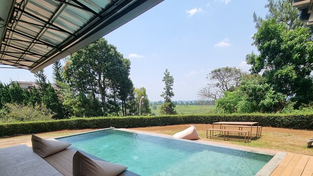 Une piscine dotée d’une terrasse en bois et d’un espace détente, entourée de verdure et d’arbres.