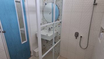 A bathroom with a blue door, a glass-enclosed shower area, a white sink, and a toilet.
