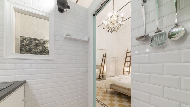 Een badkamer met witte metrotegels, een raam met uitzicht, een kroonluchter en een zwart-wit betegelde vloer.
