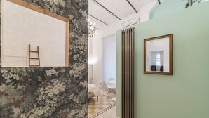 Een kamer met een bloemenbehang, een radiator, een lijst met spiegel en een geruit vloertje.