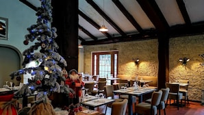 A restaurant with a Christmas tree, wooden beams, stone walls, and tables set for dining.