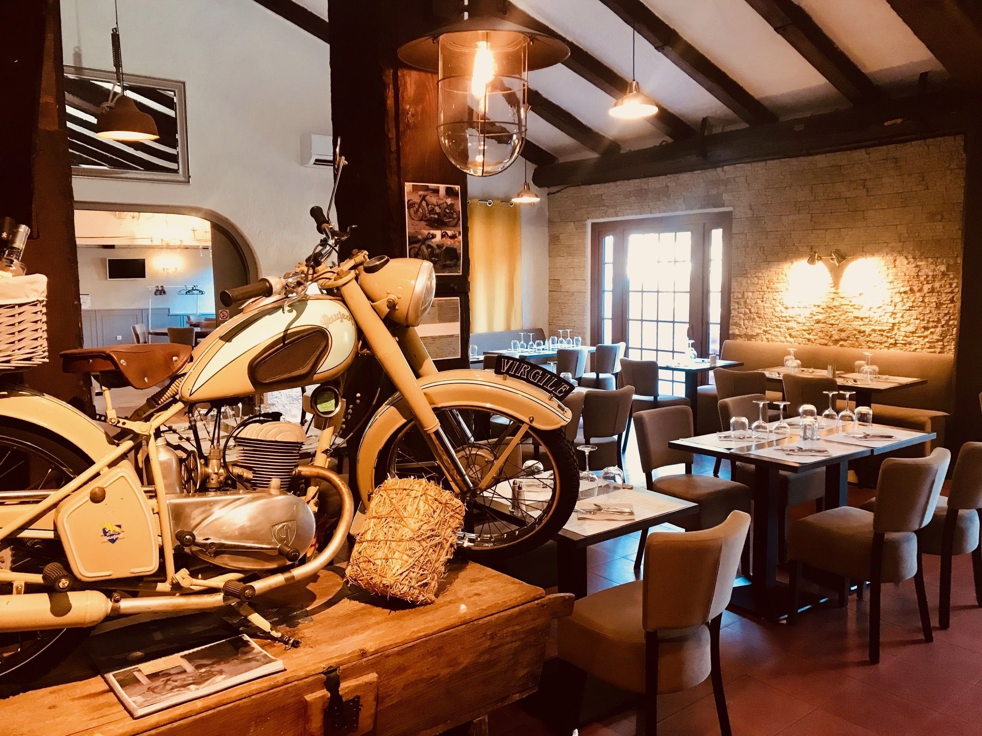 A restaurant with a vintage motorcycle centerpiece, wooden tables, and a stone wall.