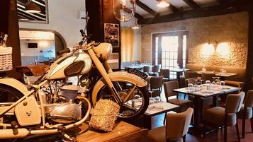 A restaurant with a vintage motorcycle centerpiece, wooden tables, and a stone wall.
