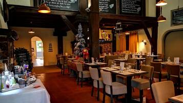 Een restaurantinterieur met gedekte tafels, een versierde kerstboom en een menubord.