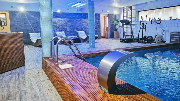 An indoor swimming pool with a wooden deck, lounge chairs, and exercise equipment.