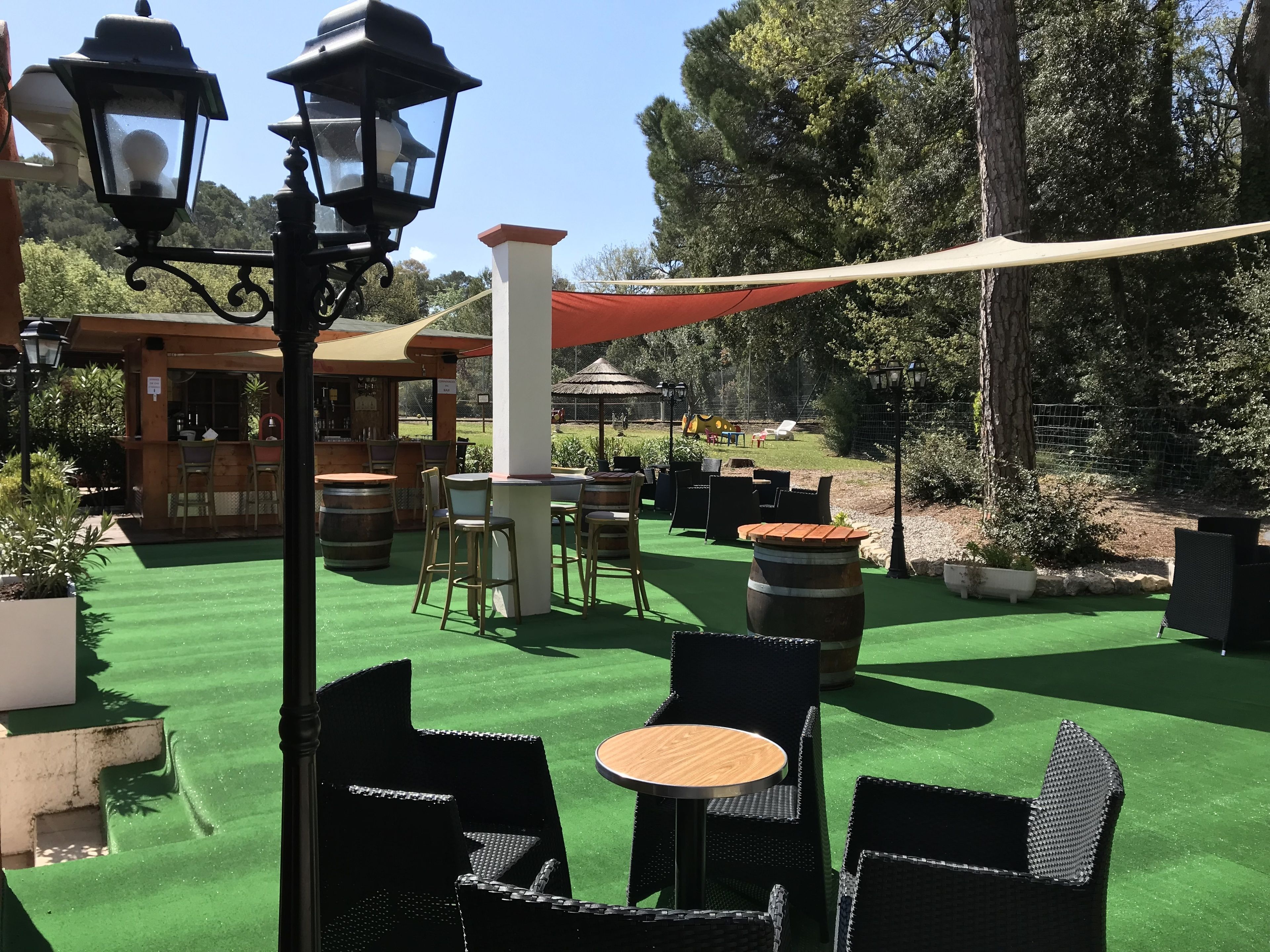 An outdoor patio area with green artificial turf, black wicker furniture, and wooden barrels.