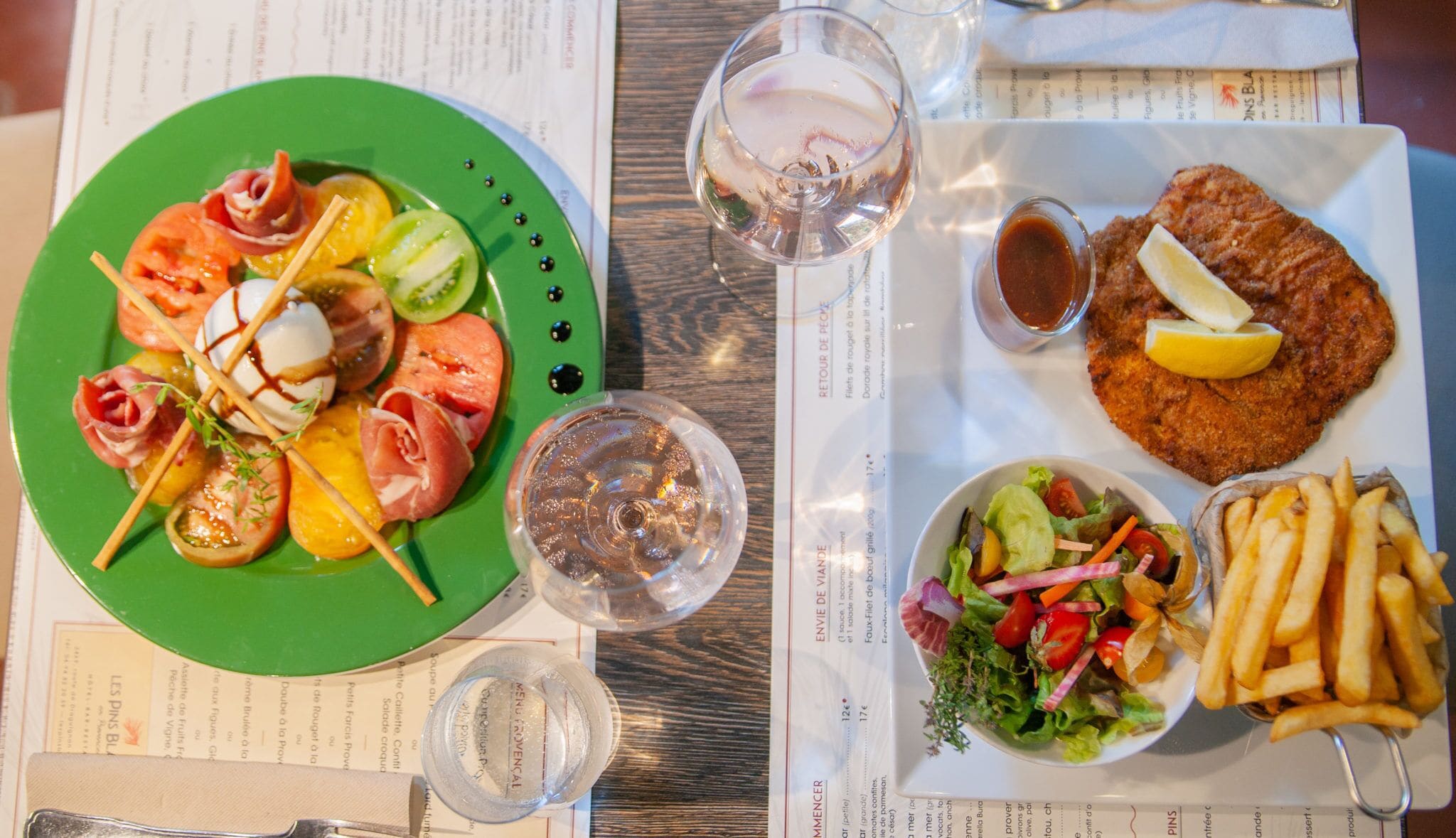 A meal with a green plate of assorted meats and vegetables, a glass of water, a fried fish dish, a salad, and fries.