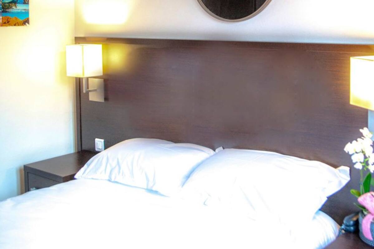 A hotel room with a bed, two bedside lamps, and a nightstand with a plant.