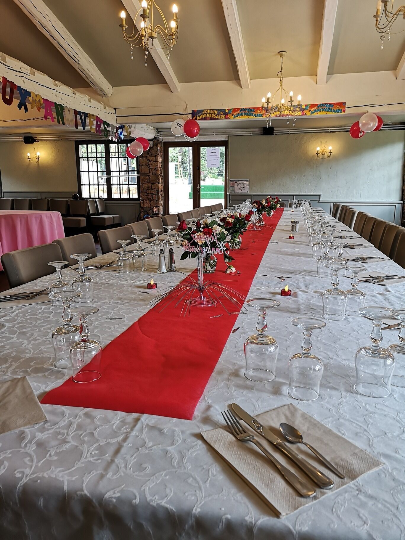 Un salón de banquetes con una larga mesa dispuesta para un evento formal, con una alfombra roja, cristalería y centros de mesa florales.