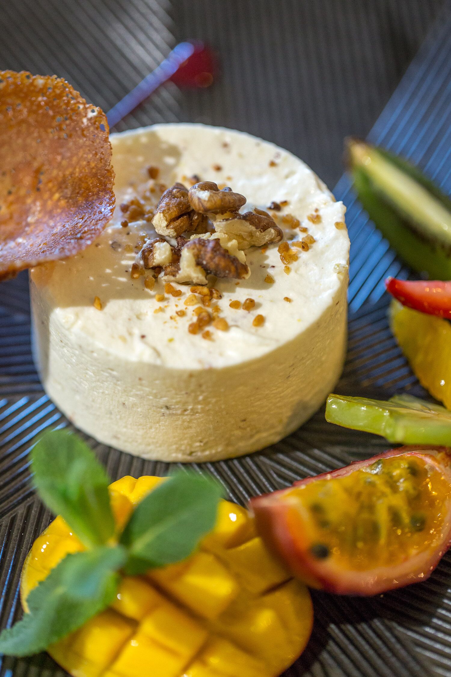 A dessert with a creamy topping, garnished with nuts and a crispy element, surrounded by fruit slices.