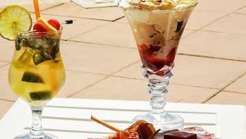 Dos bebidas sobre una mesa junto a una piscina, con diversos tipos de carne y encurtidos.