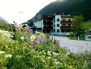 A hotel with a mountain backdrop, featuring a road in the foreground and lush greenery.