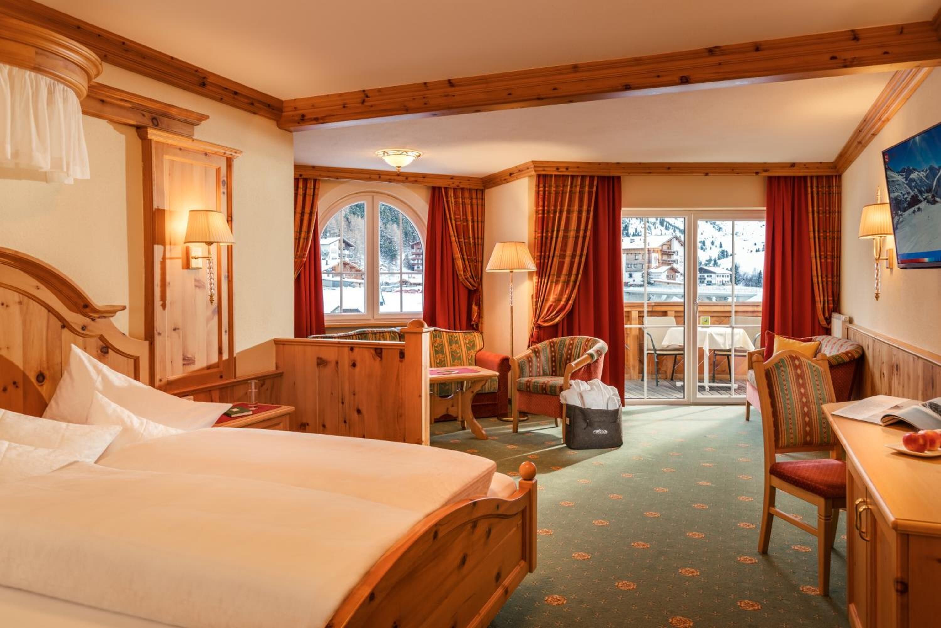Ein Hotelzimmer mit einem hölzernen Bett, einem Schreibtisch, einem Stuhl und Blick auf einen verschneiten Berg.