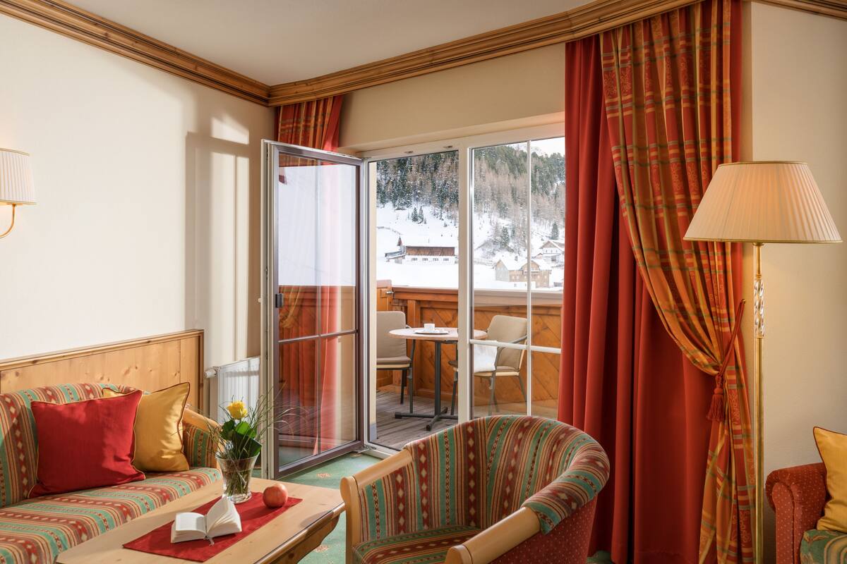 A cozy room with a sofa, a table with a book and a vase, and a view of a snowy landscape through a glass door.