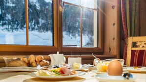 A breakfast table with croissants, eggs, and a view of a snowy forest through large windows. - Hotel Venter Bergwelt (Soelden)