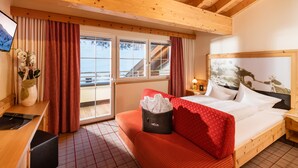 A room with a wooden ceiling, a bed with white bedding, a red sofa, a wooden desk, and a window with curtains. - Hotel Venter Bergwelt (Soelden)