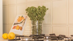 Una cocina con estufa a gas, un florero de vidrio con hierbas verdes y un libro de cocina en la encimera.