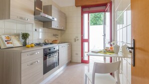 Una cocina moderna con estufa a gas, horno y campana extractora de acero inoxidable. Hay un comedor con una silla blanca y una mesa lista para el desayuno.