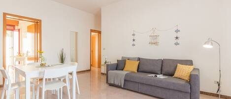 A spacious living area with a grey sofa, white chairs, and a dining table.