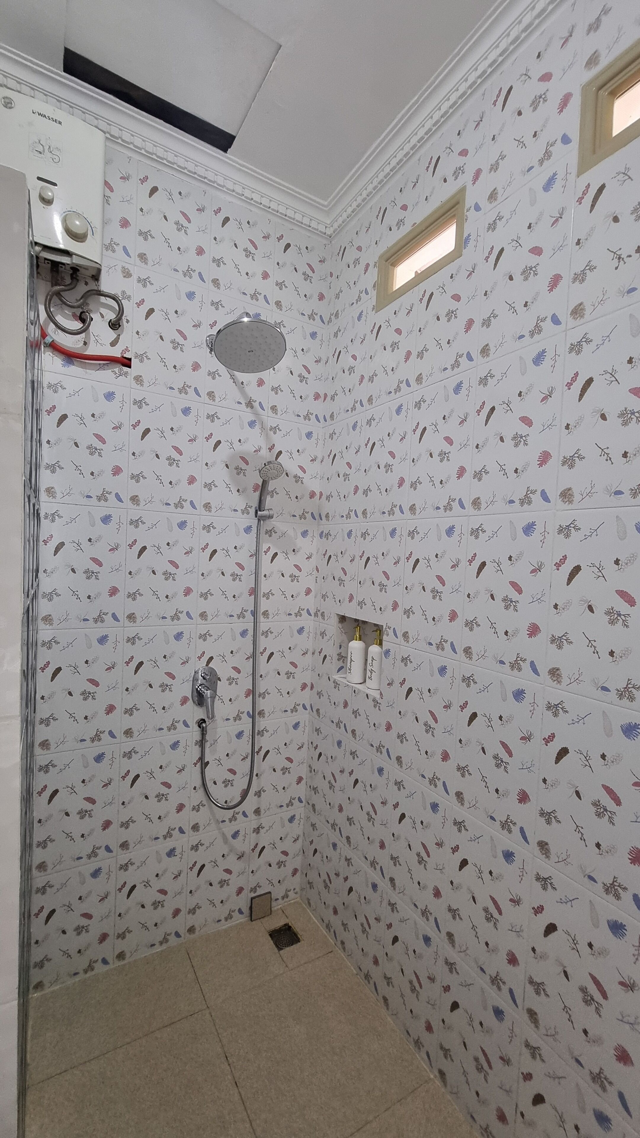 A shower with floral patterned tiles, a handheld showerhead, and a wall-mounted faucet.