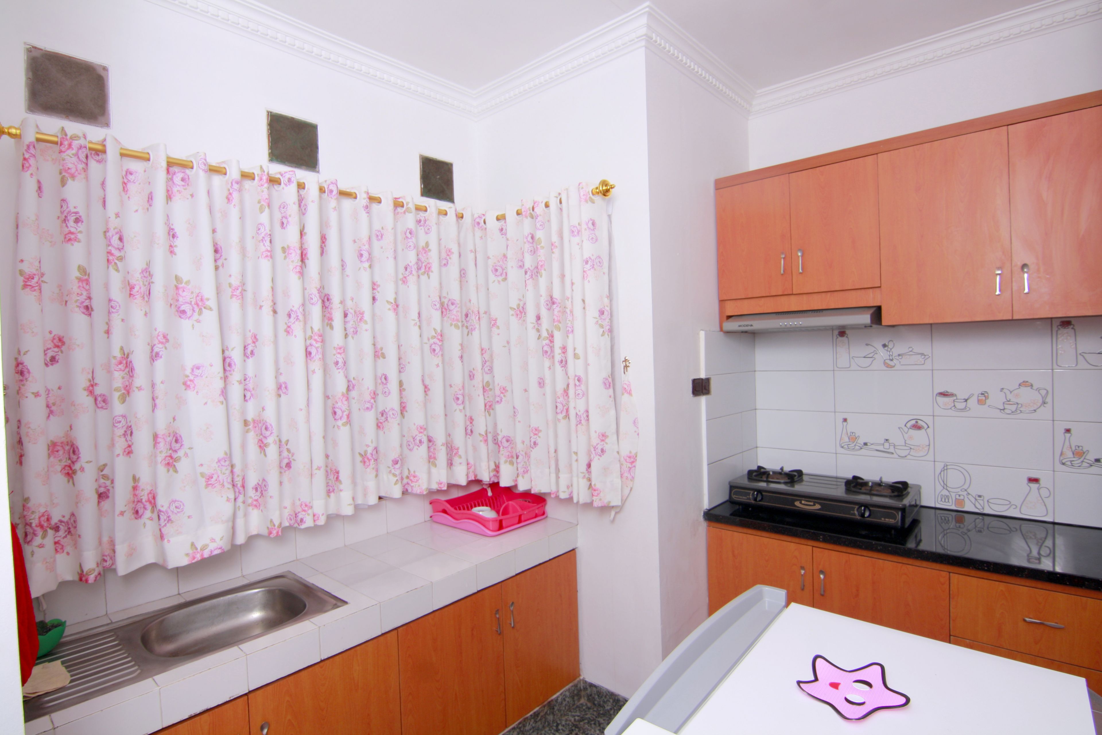 Una cocina con armarios de madera, un lavamanos de acero inoxidable y un salpicadero de azulejos con dibujos.