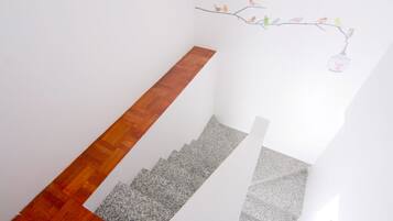 Una escalera con escalones de madera y granito, paredes blancas y un adorno de aves en una rama.