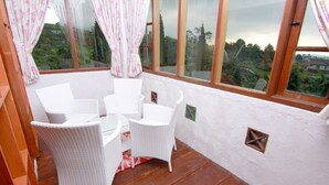 Ein Zimmer mit Holzboden, weißen Korbmöbeln und großen Fenstern mit Vorhängen.