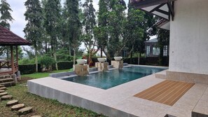 A rectangular swimming pool with a stone border, surrounded by a wooden deck and a small garden area. - Villa ChavaMinerva Dima - Ciater (Ciater)