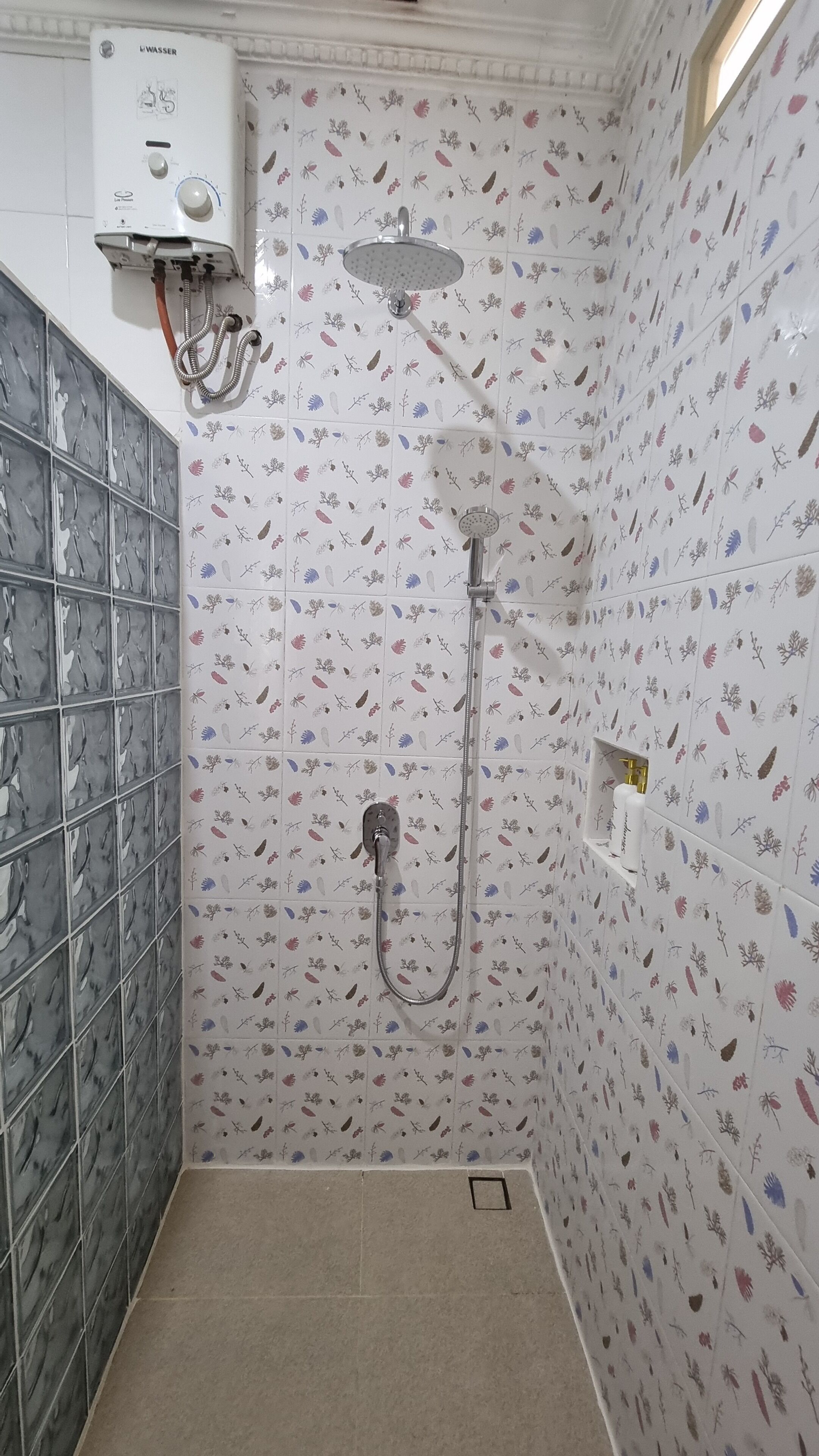 A shower room with a water heater, a showerhead, and a hand shower.