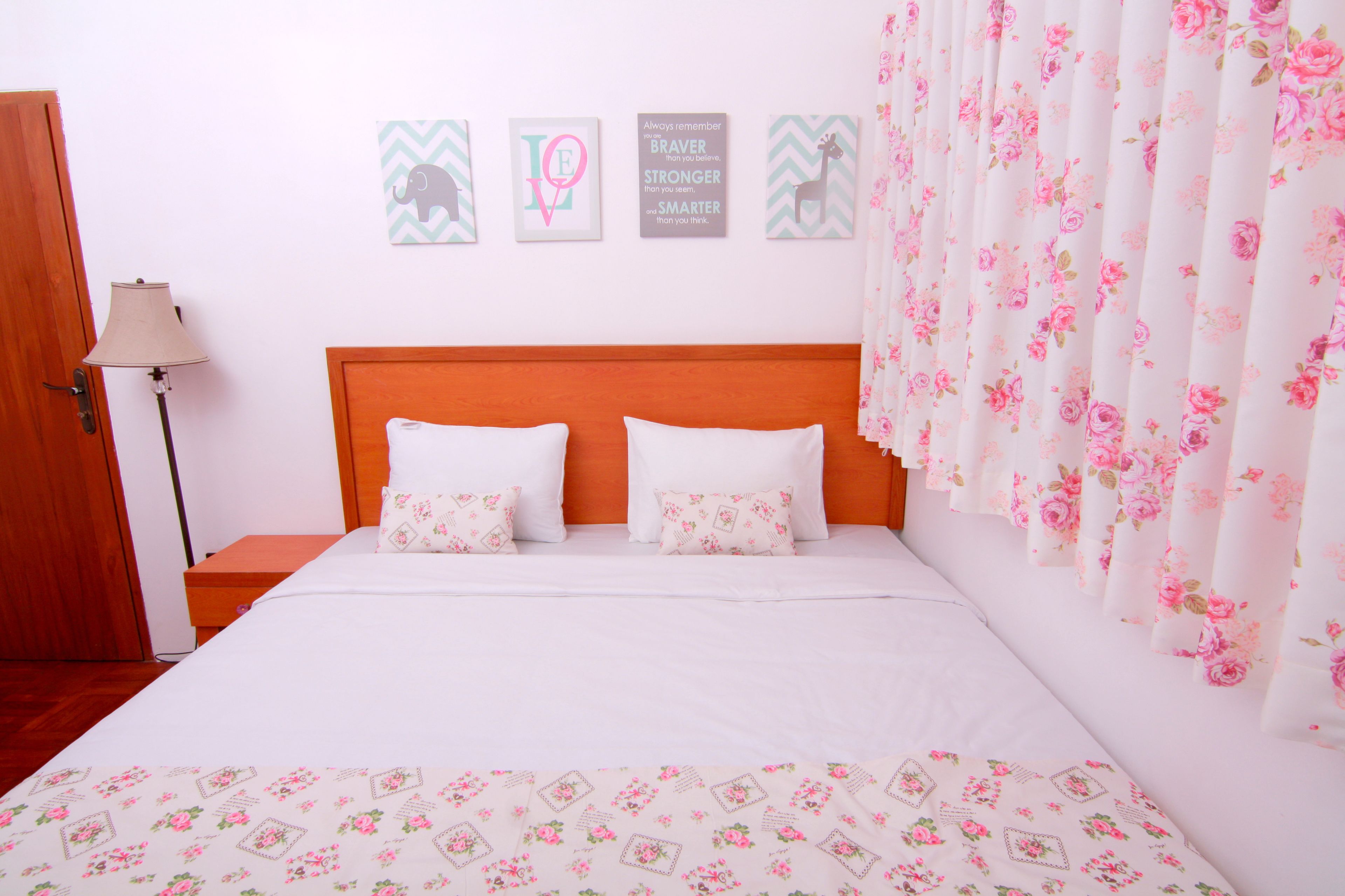 A neatly made bed with white bedding and floral-patterned pillows, a wooden headboard, and a wall with motivational quotes and a cheetah picture.