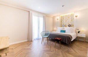 Un dormitorio moderno con suelo de madera estampada, una cama con ropa de cama blanca, una silla azul y una mesita de noche con lámpara.