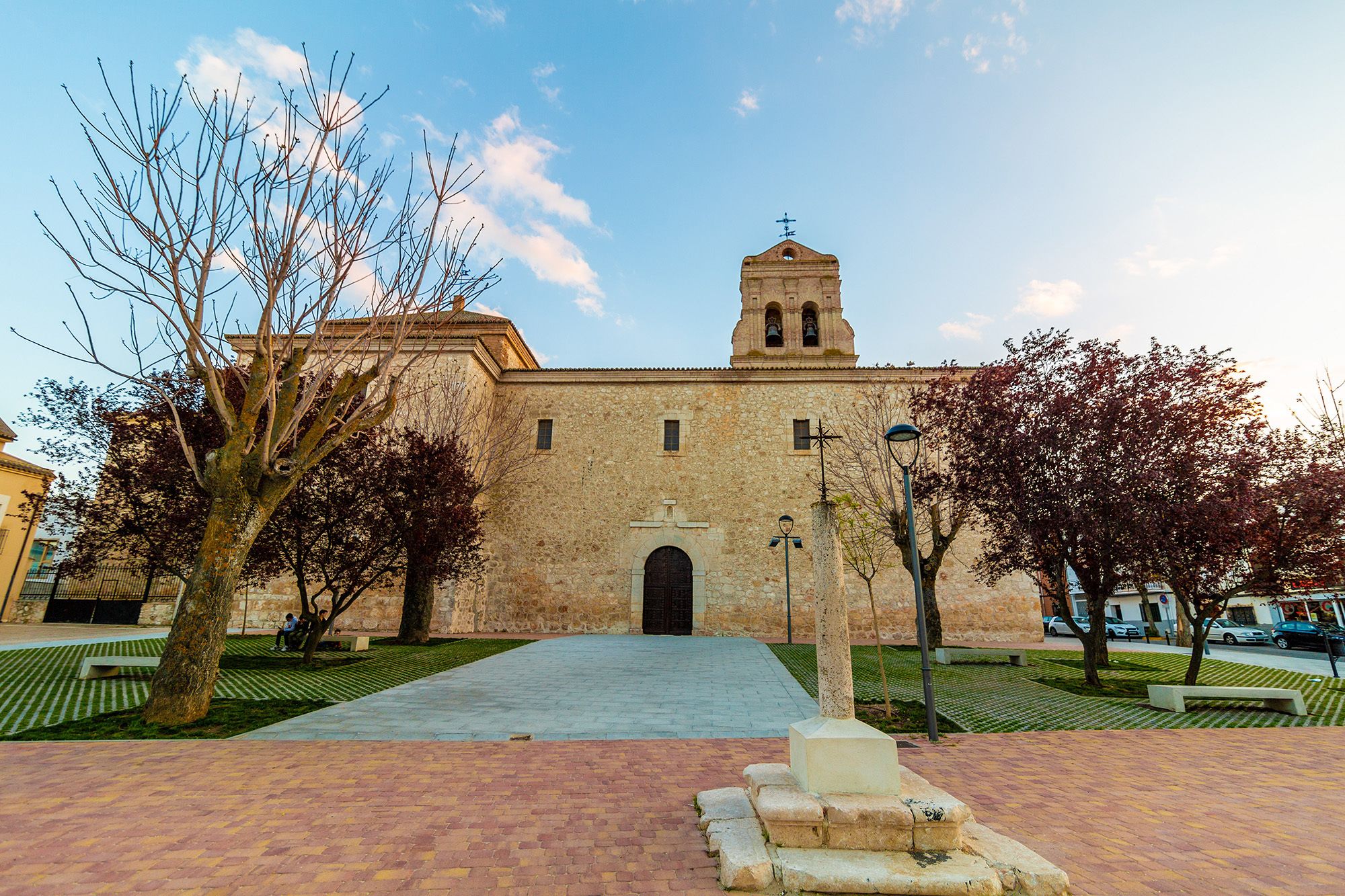 Edificio histórico con una torre de campanas, patio empedrado y árboles circundantes.